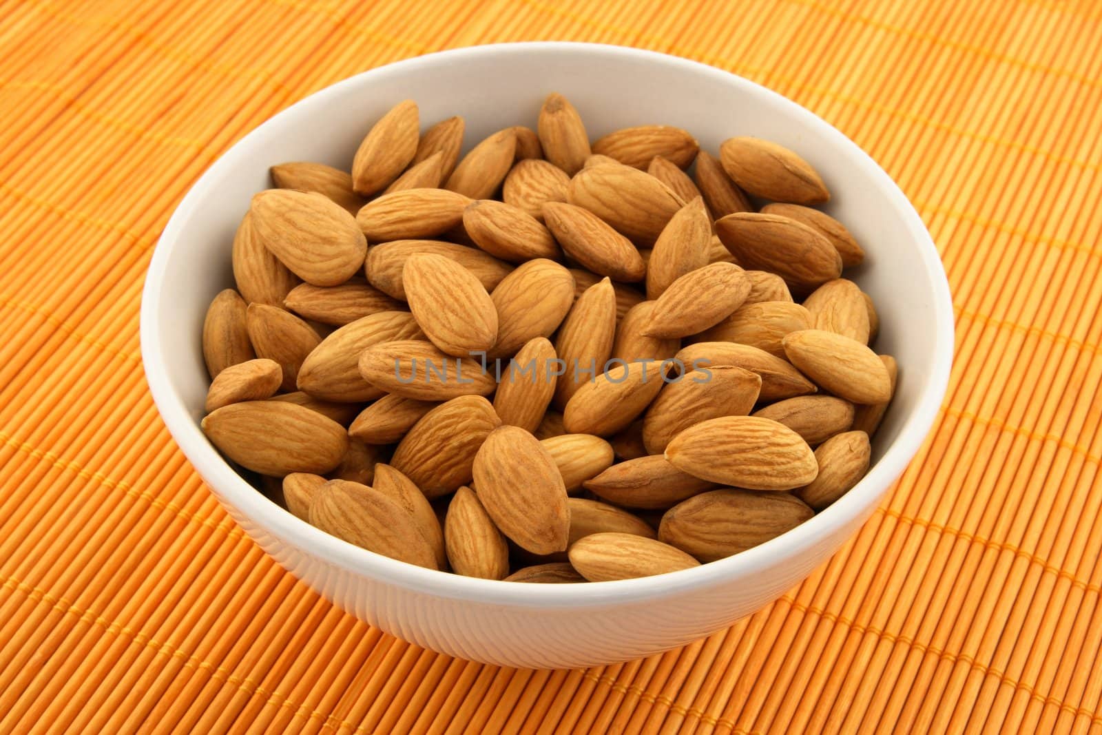 Fresh almonds in a bowl on orange rattan mat.