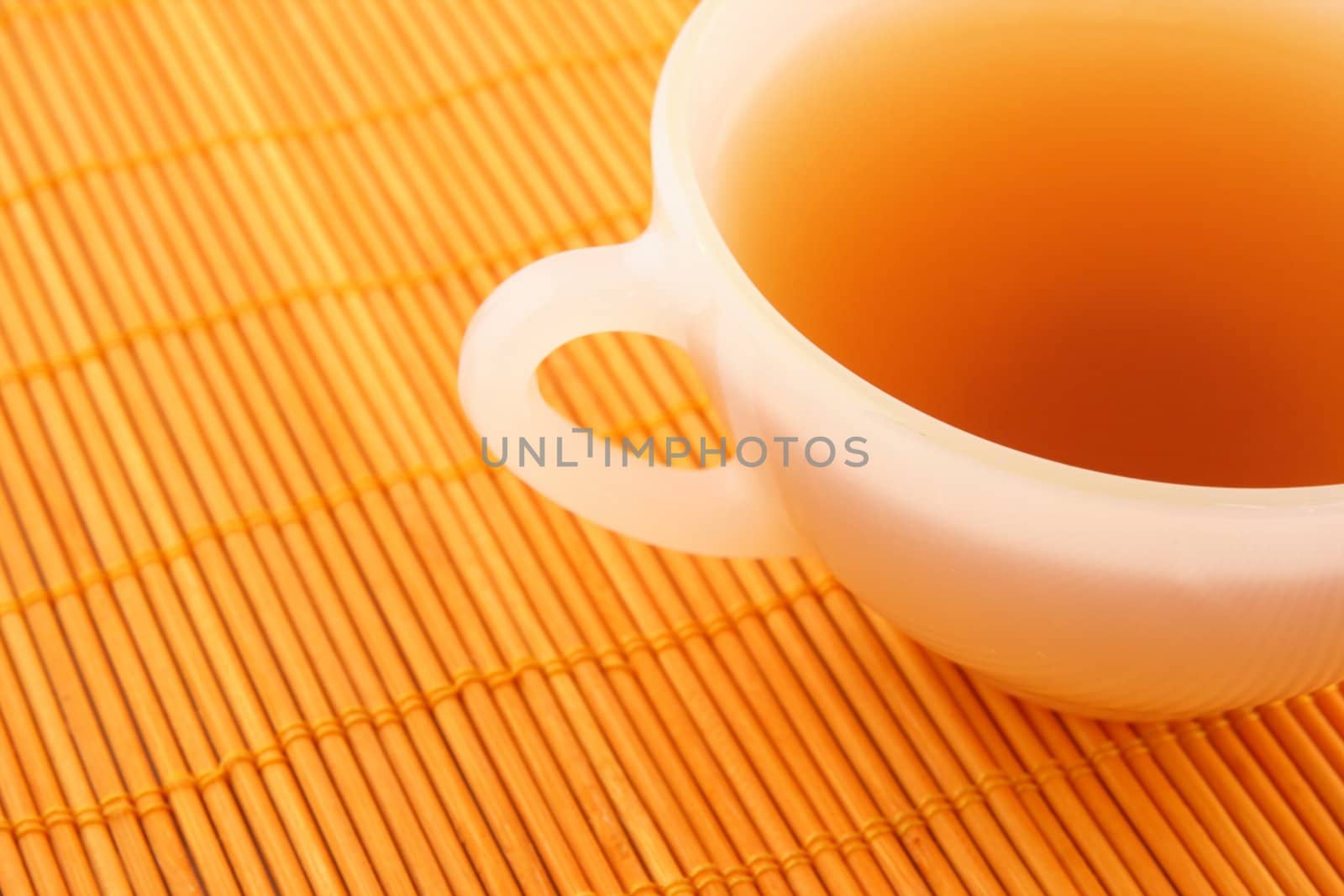 Cup of tea on orange rattan mat in warm colors.