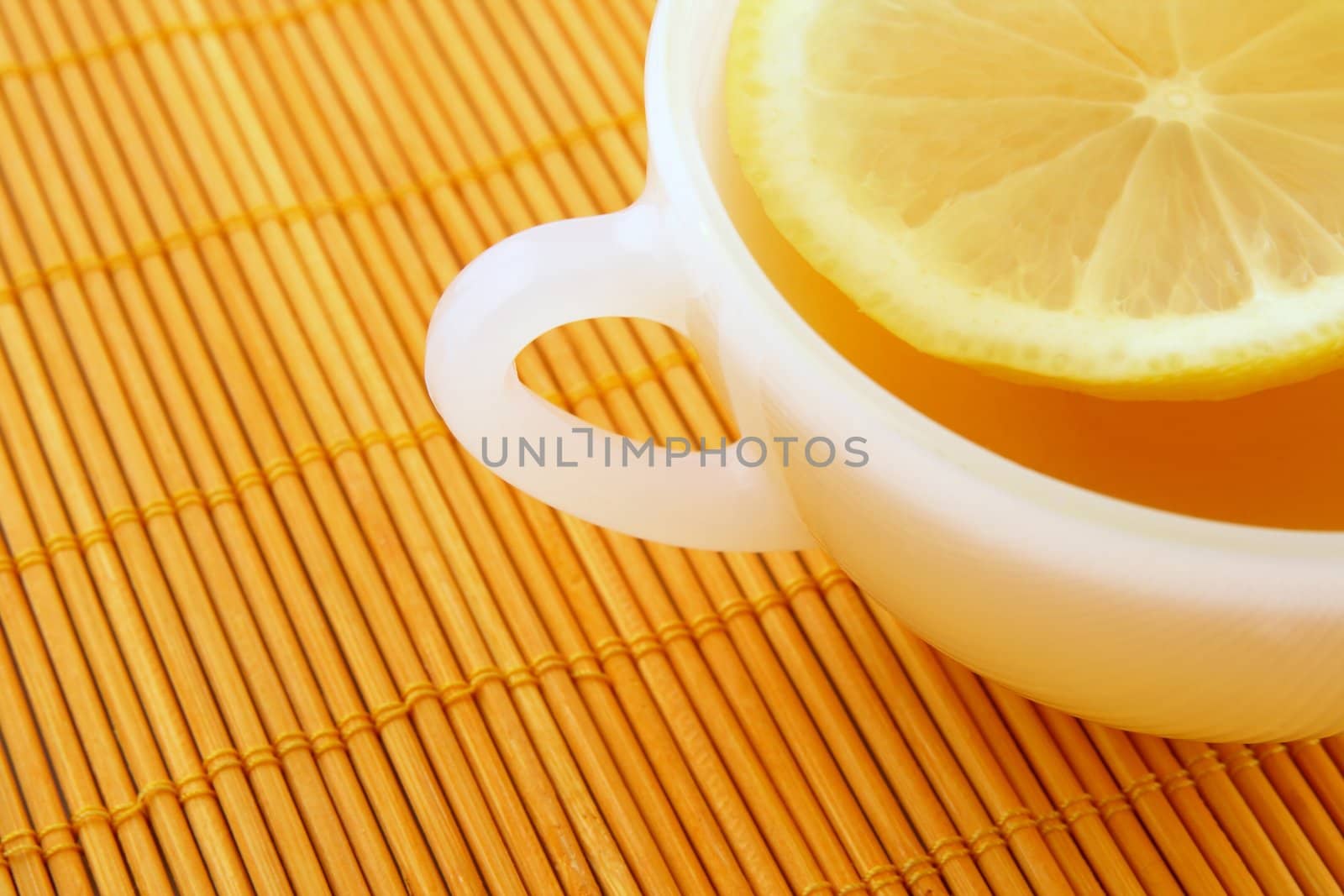 Teatime. Cup of tea with lemon on orange rattan mat.