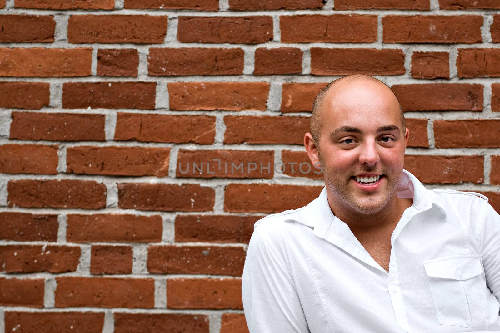 A happy and cheerful young man posing outdoors in front of a brick wall with copyspace.