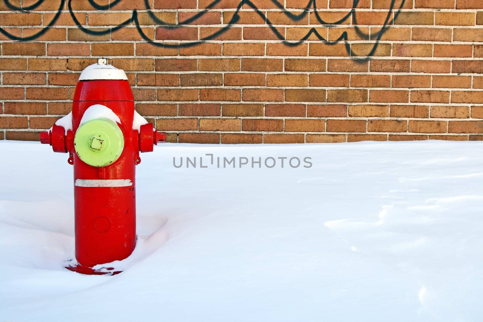 Red fire hydrant in the snow, near a brick building.