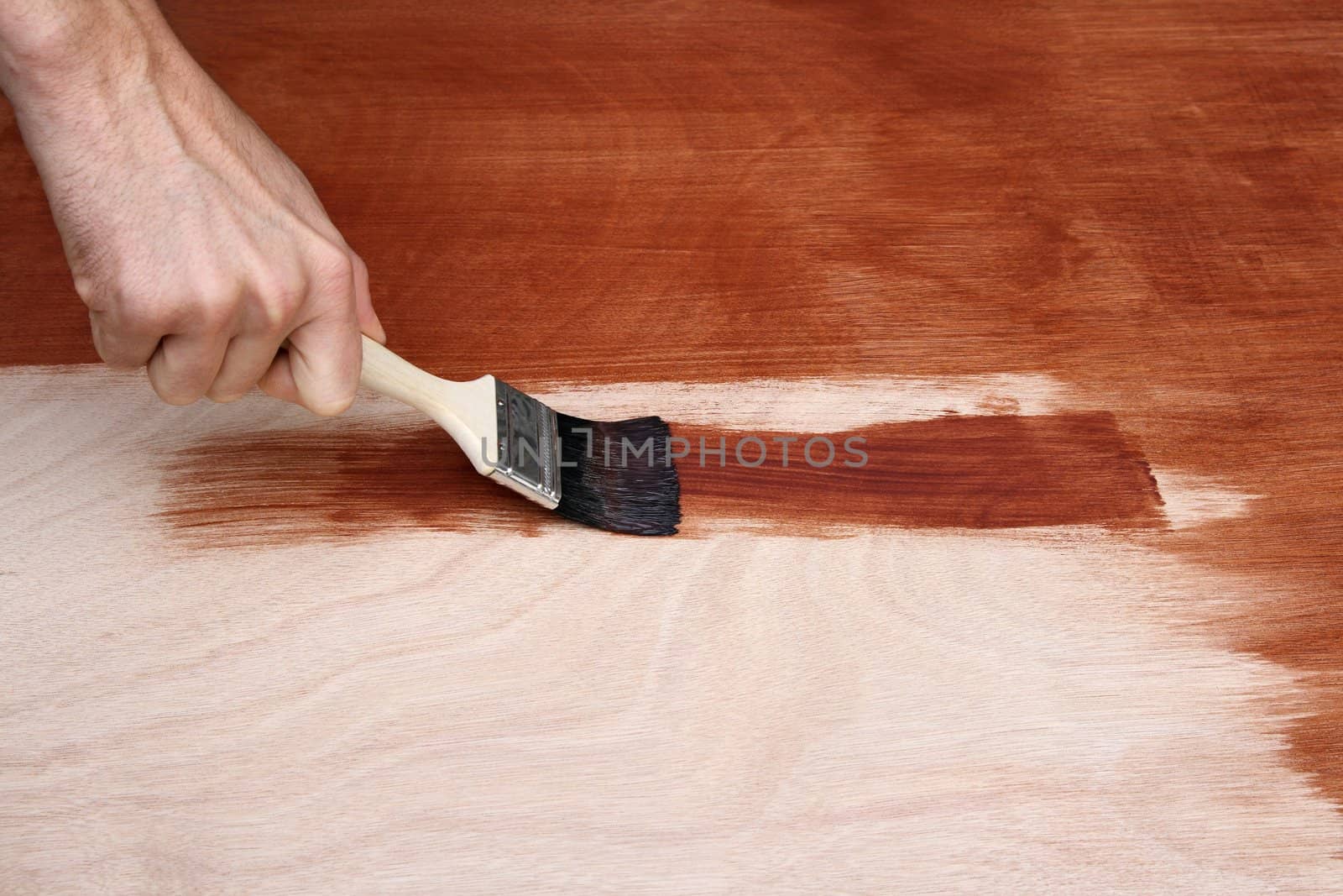 Man's hand painting a wooden surface with a brush.