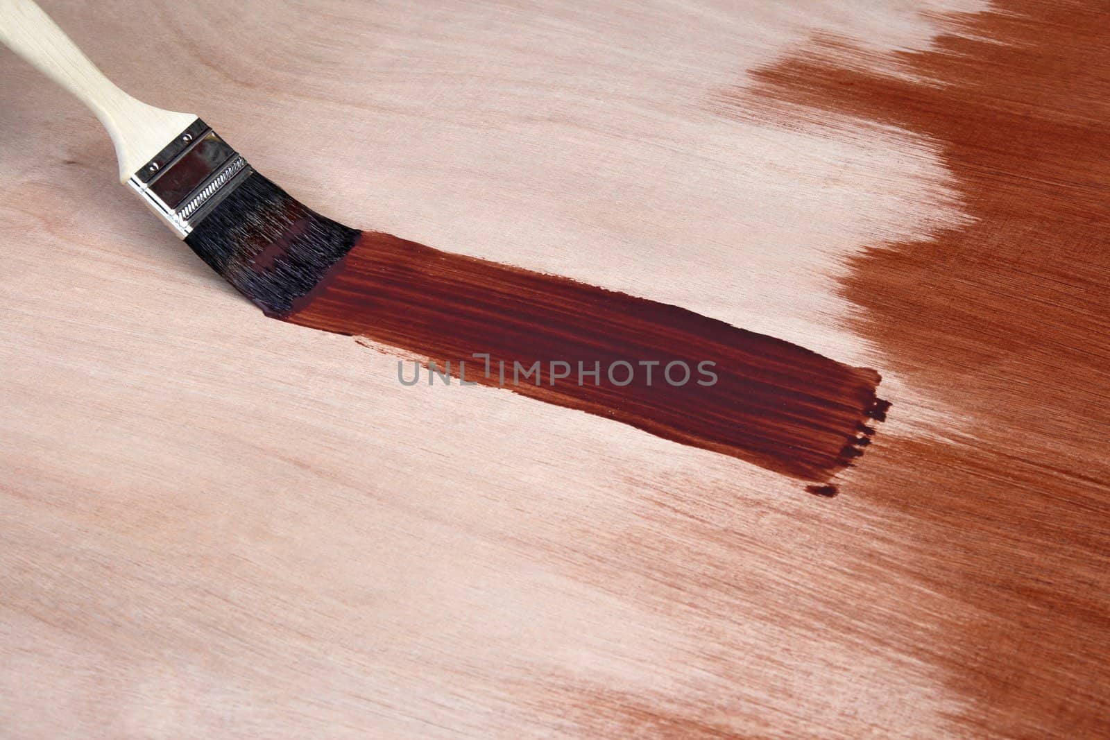 Paintbrush leaving a fresh brush stroke on wooden surface.