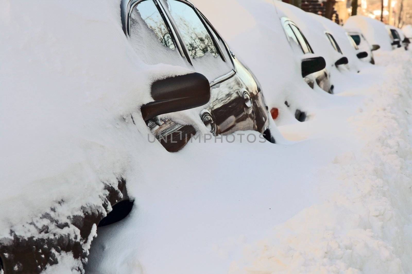 Row of cars covered by deep snow. Urban street after the heavy snowstorm.