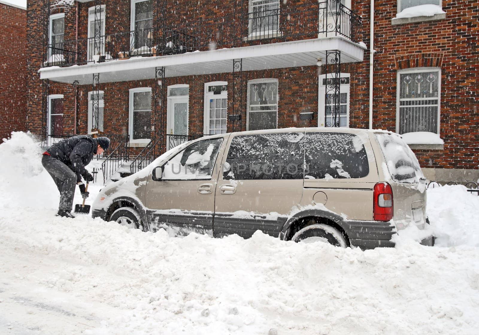 Man shovelling and removing snow from his car during a heavy snow storm.