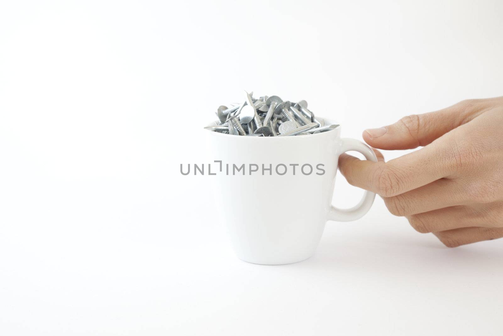 A woman picks up a coffee cup full of nails on a white background.