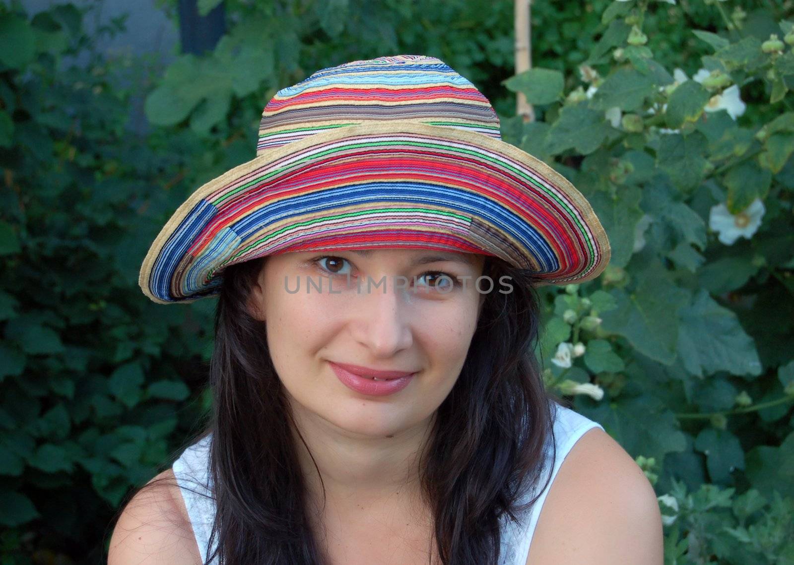 attractive young brunette in colorful hat against green leaves in the garden