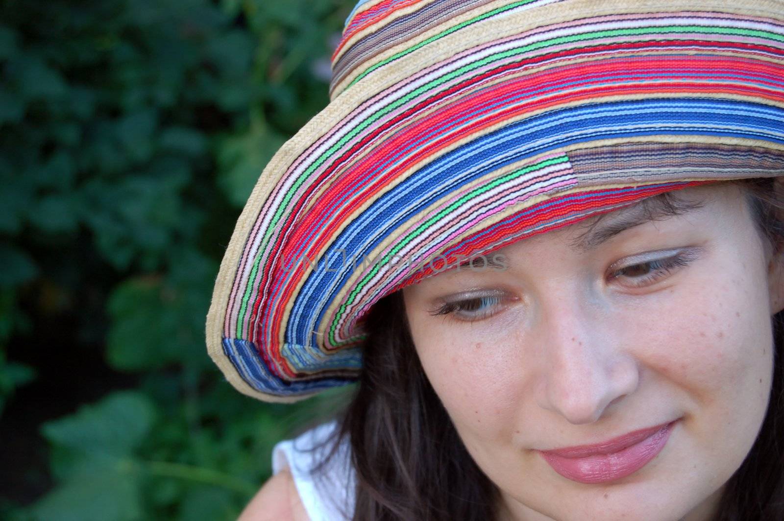 close-up of attractive young brunette in colorful hat against green leaves in the garden