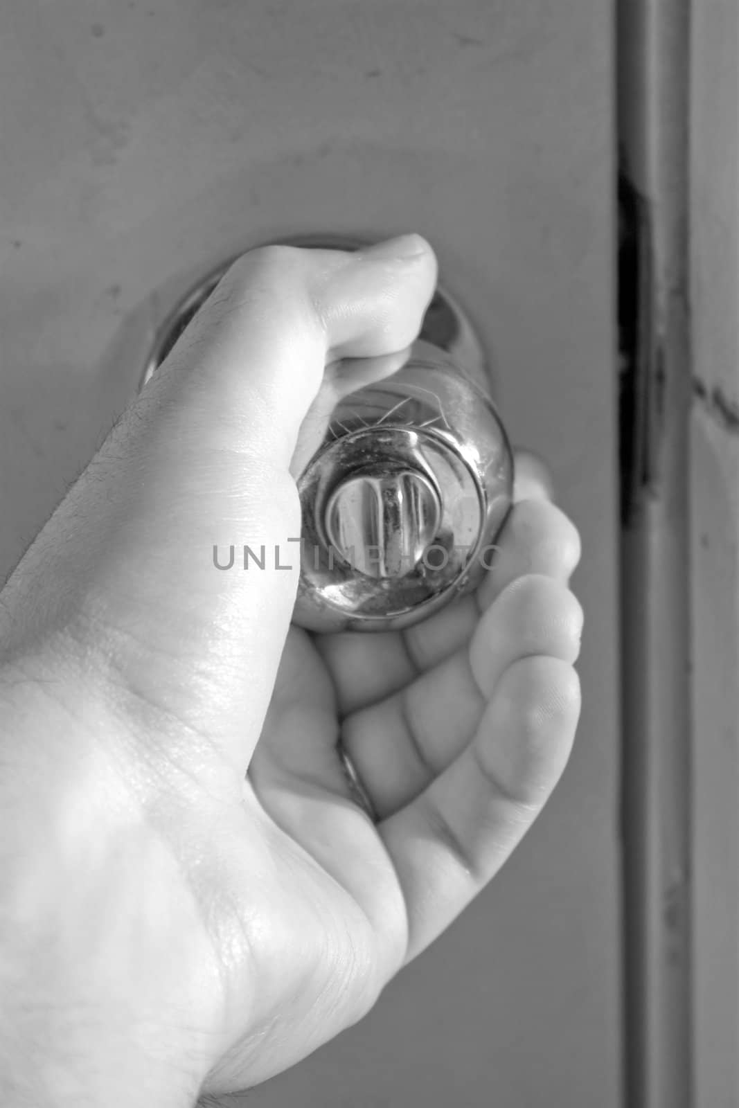 A hand grasping a shiny doorknob in black and white.