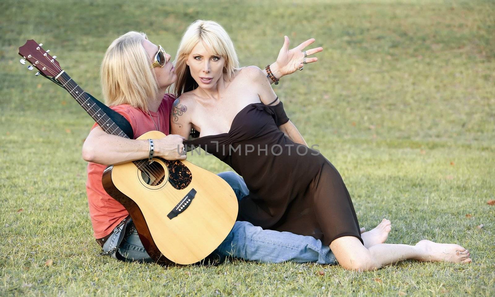 Hip adult couple with a guitar outside on grass