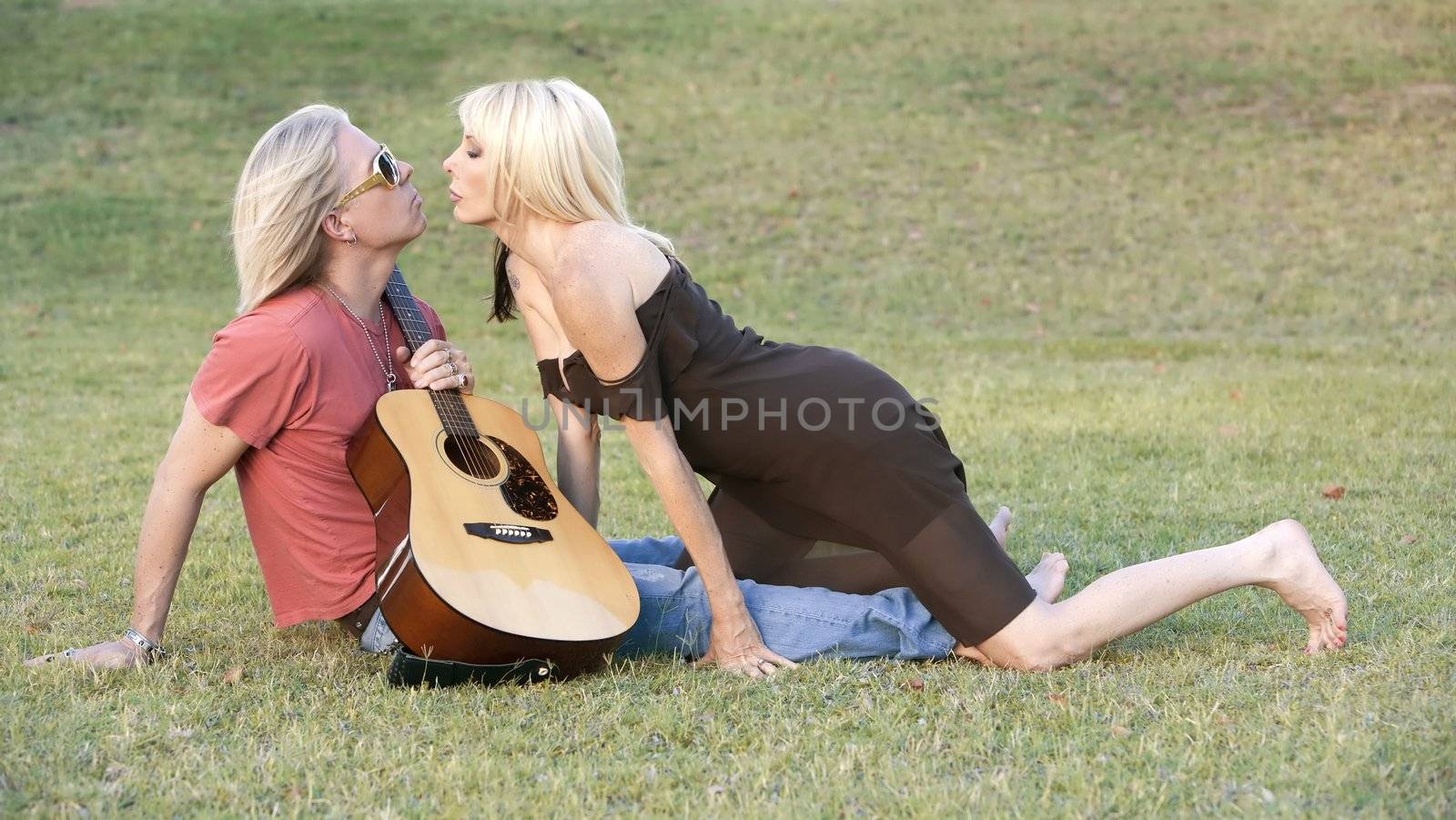 Hip adult couple with a guitar outside on grass