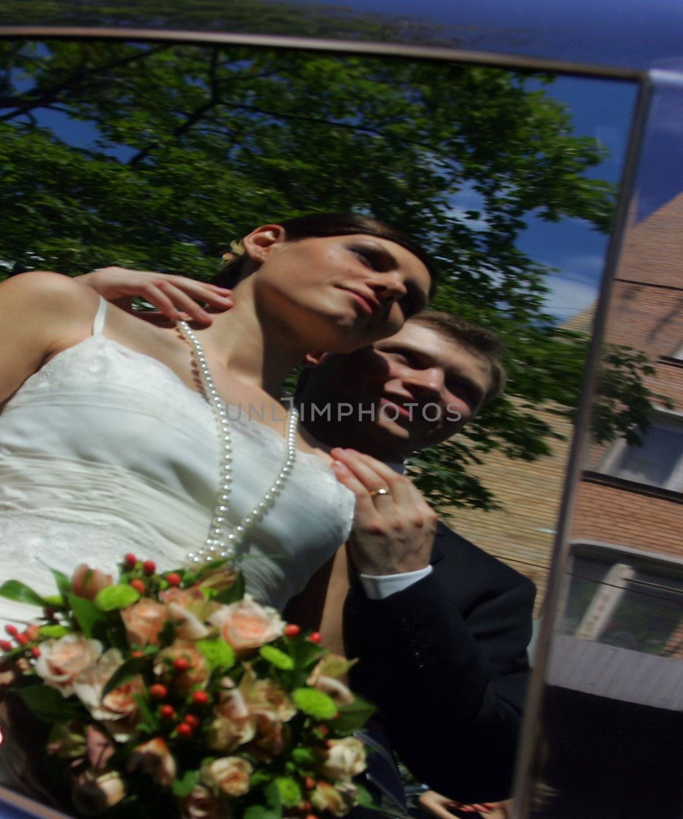 Reflection of newlywed couple in window of motor car.