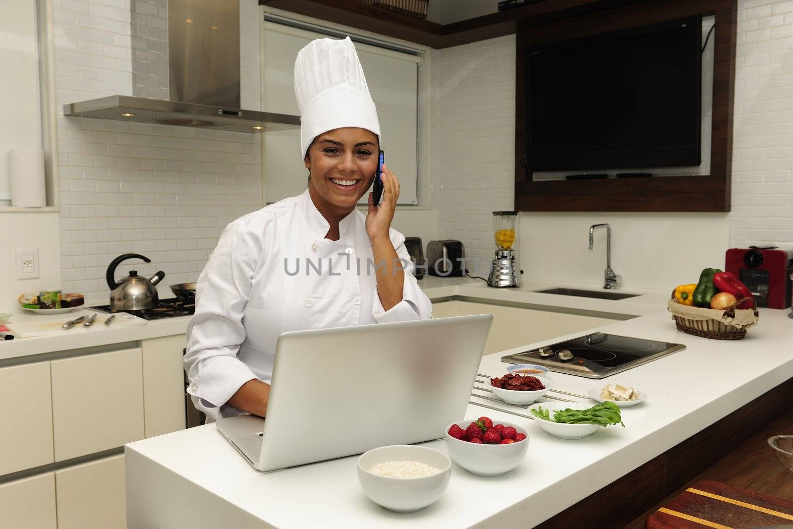 Chef cooking in kitchen talking on phone and using laptop