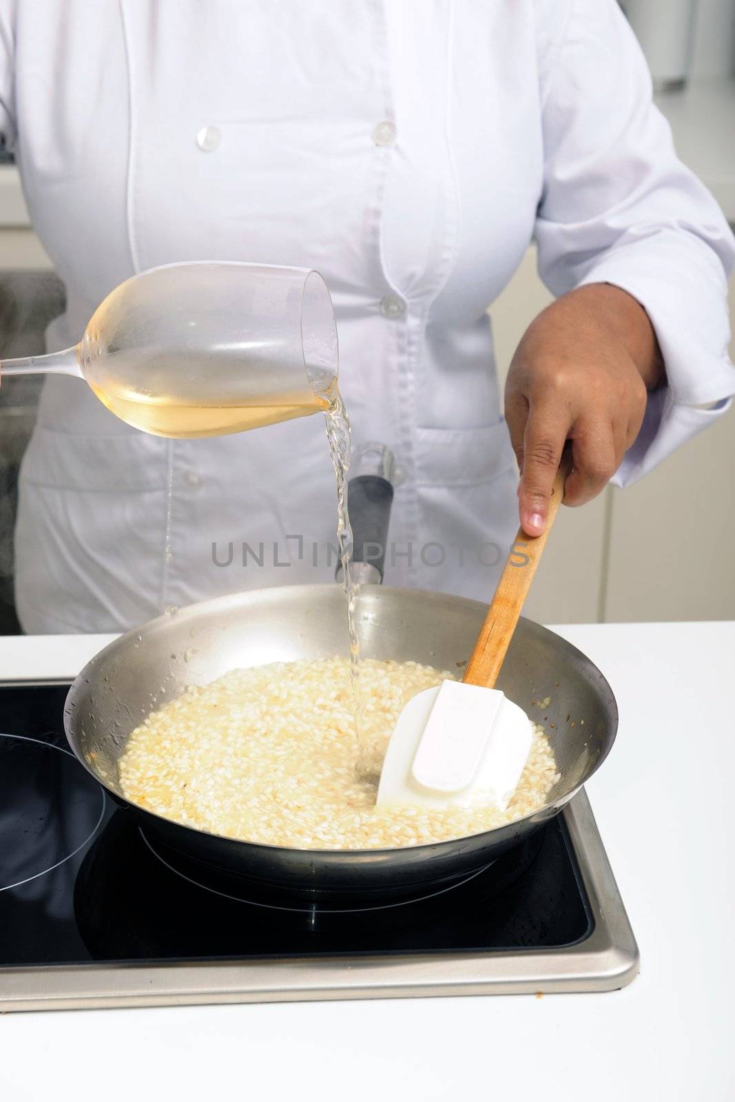 Chef cooking risotto pouring white wine into the pan