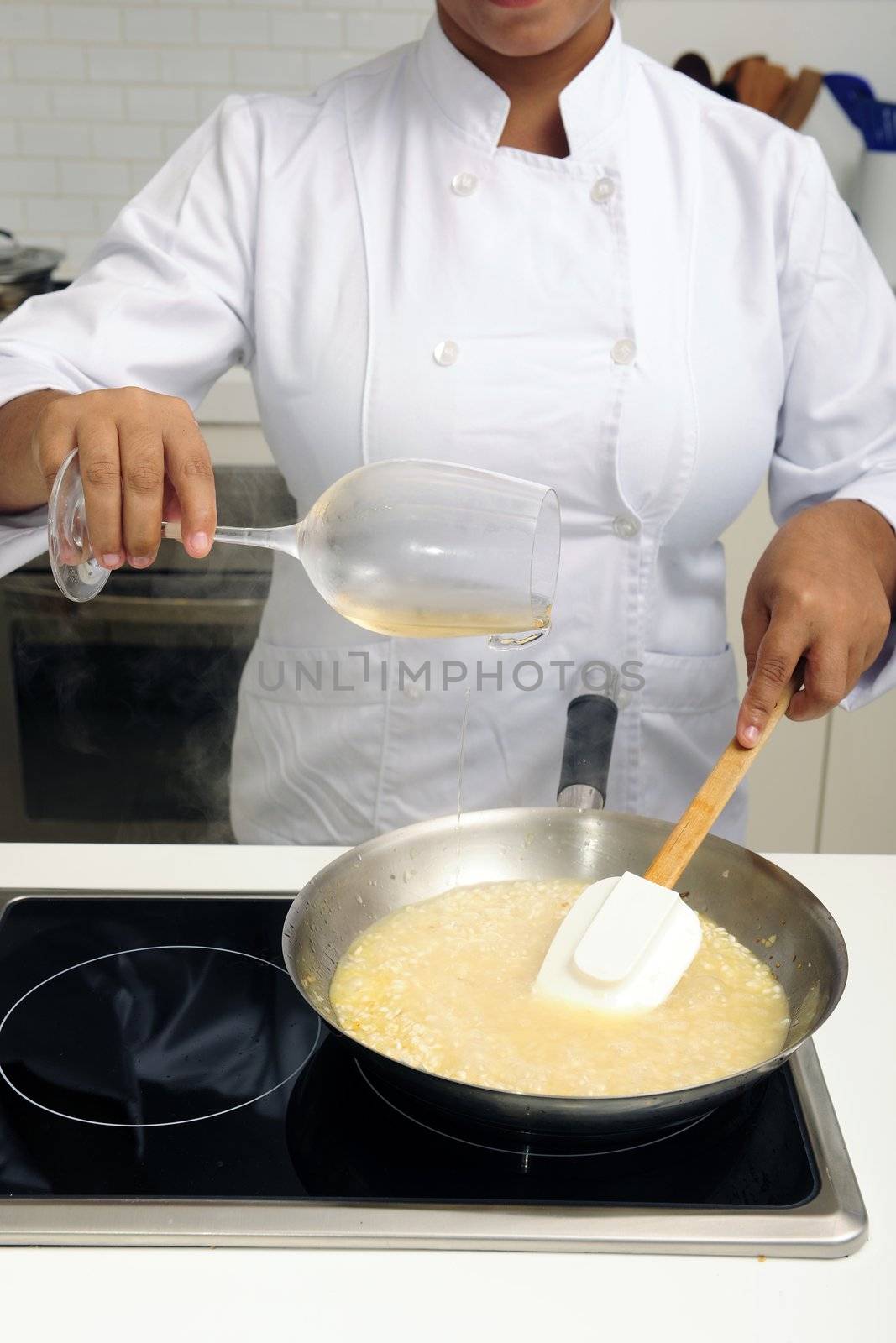 Chef cooking risotto pouring white wine into the pan