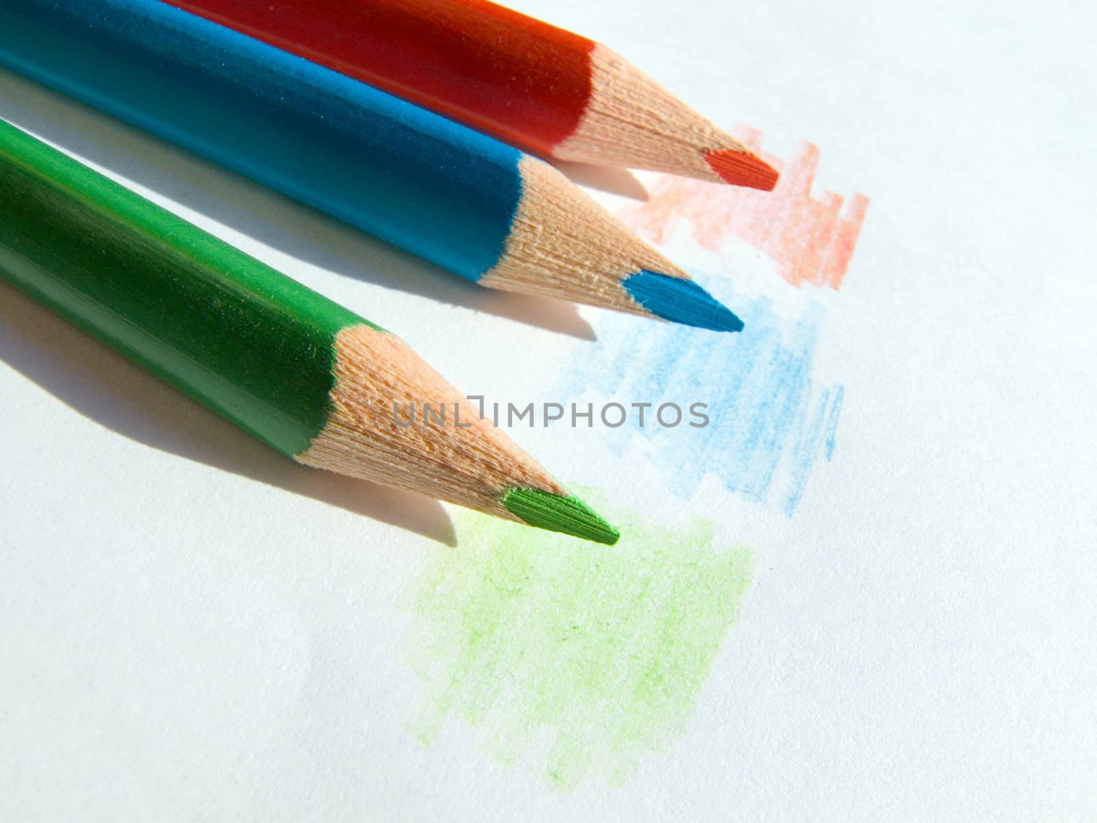 Three colored pencils on white paper sheet