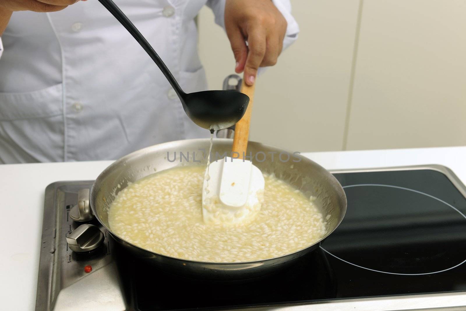 Chef cooking risotto adding stock and stirring