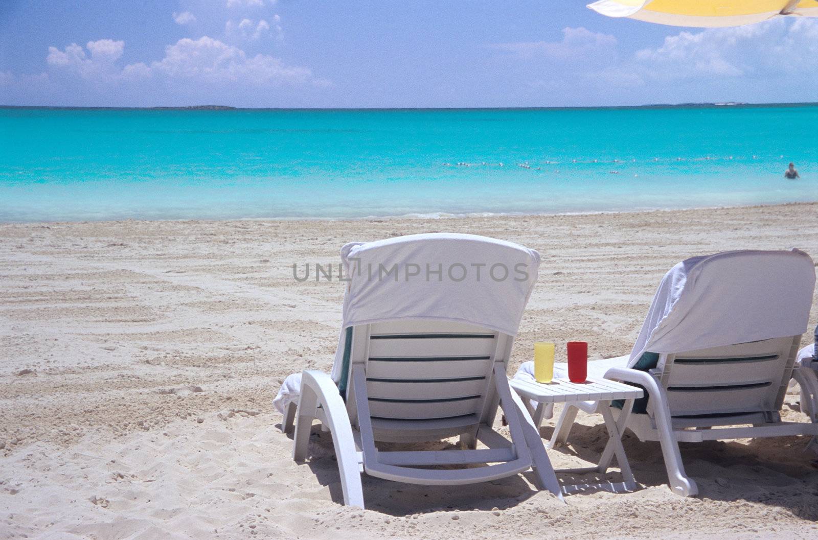 Empty deck chairs wait on a white sandy beach facing the turquoise waters of the Bahamas.