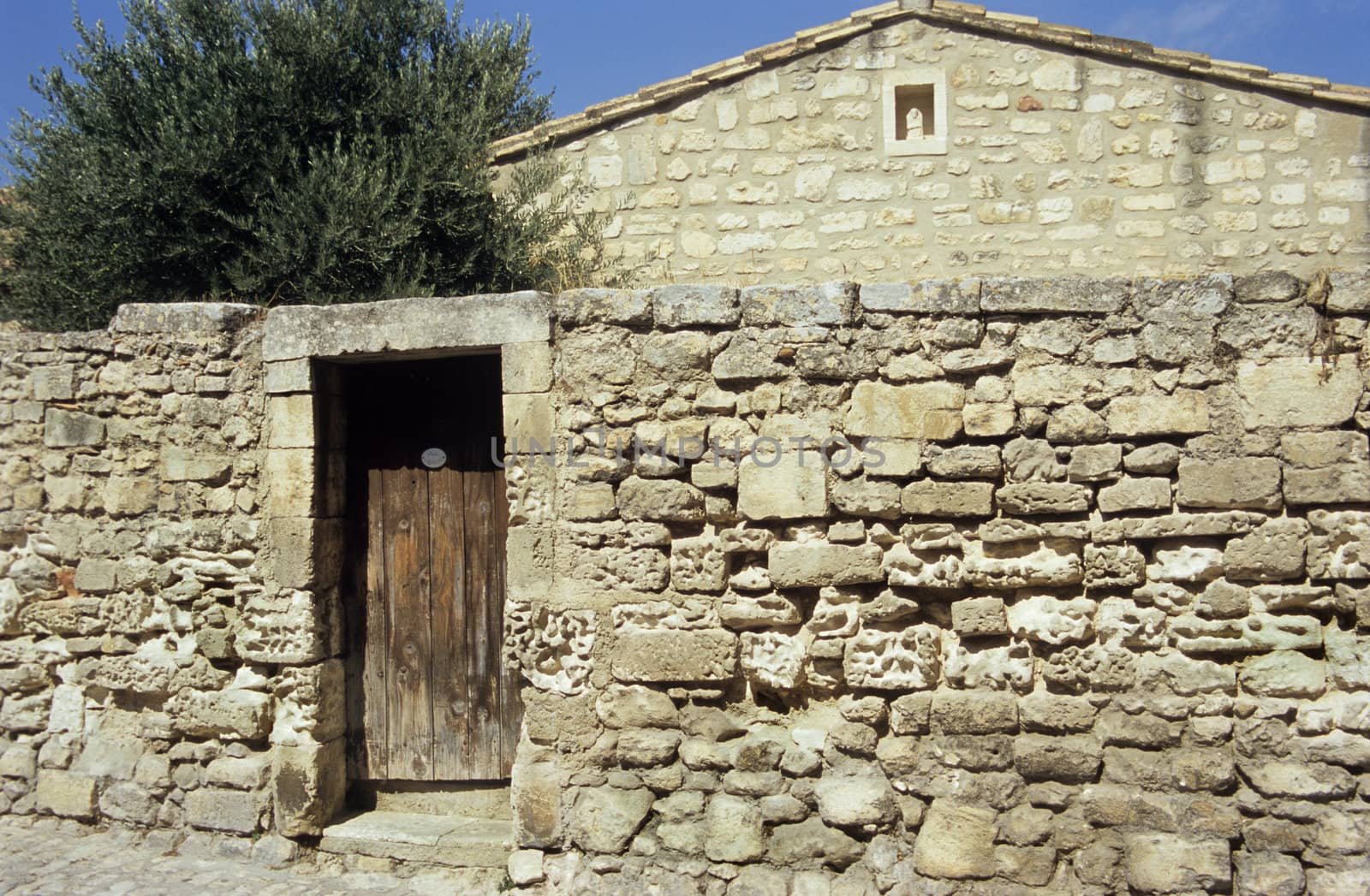 An ancient stone wall with a wooden door leading to a stone house, Les Baux de Provence, France. 