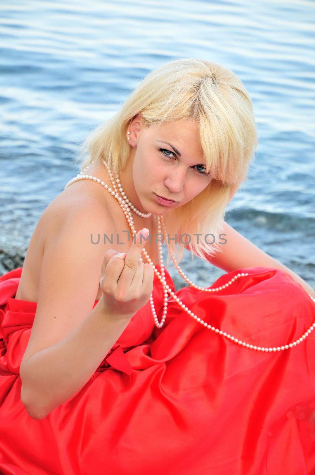 glamour  blond girl is sitting on the beach and  showing her middle finger