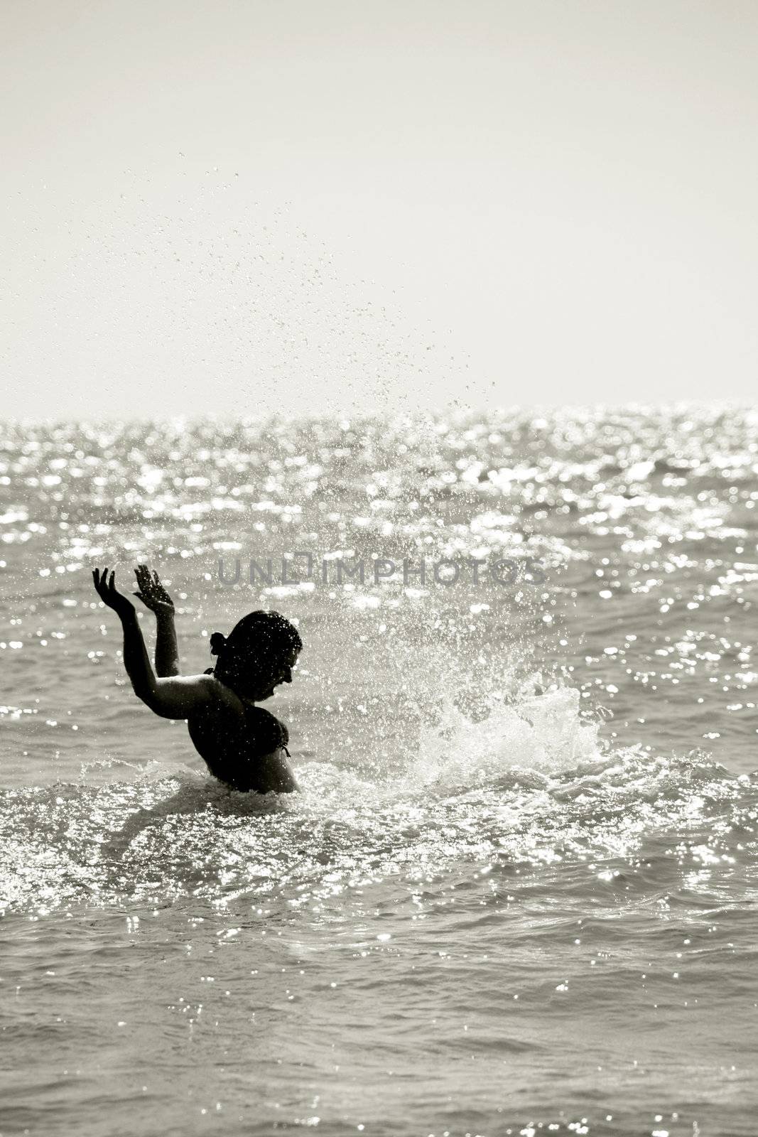 silhouette of a wet young woman in a waving sea splashing the water, vertical