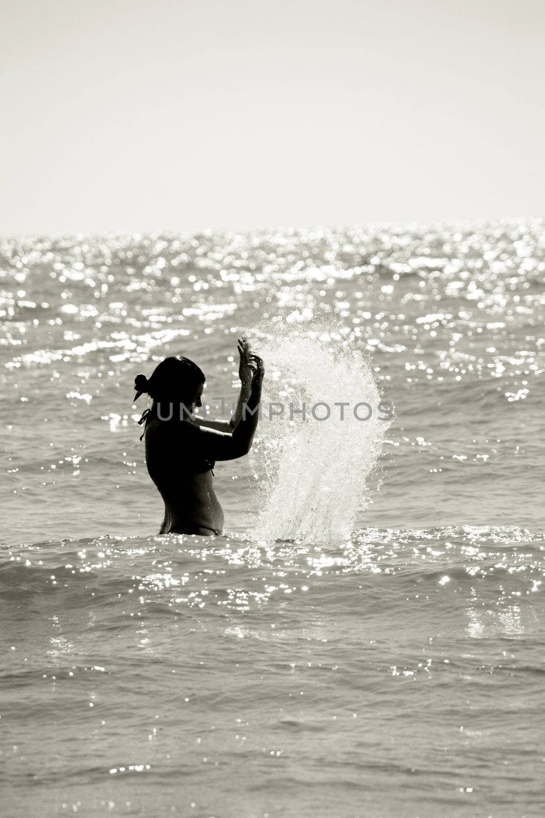 silhouette of a wet young woman in a waving sea splashing the water, vertical