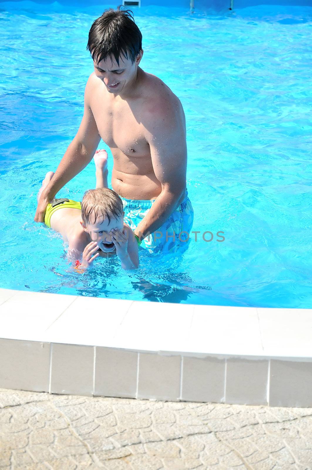 father teaching his little son to swim, boy is laughing
