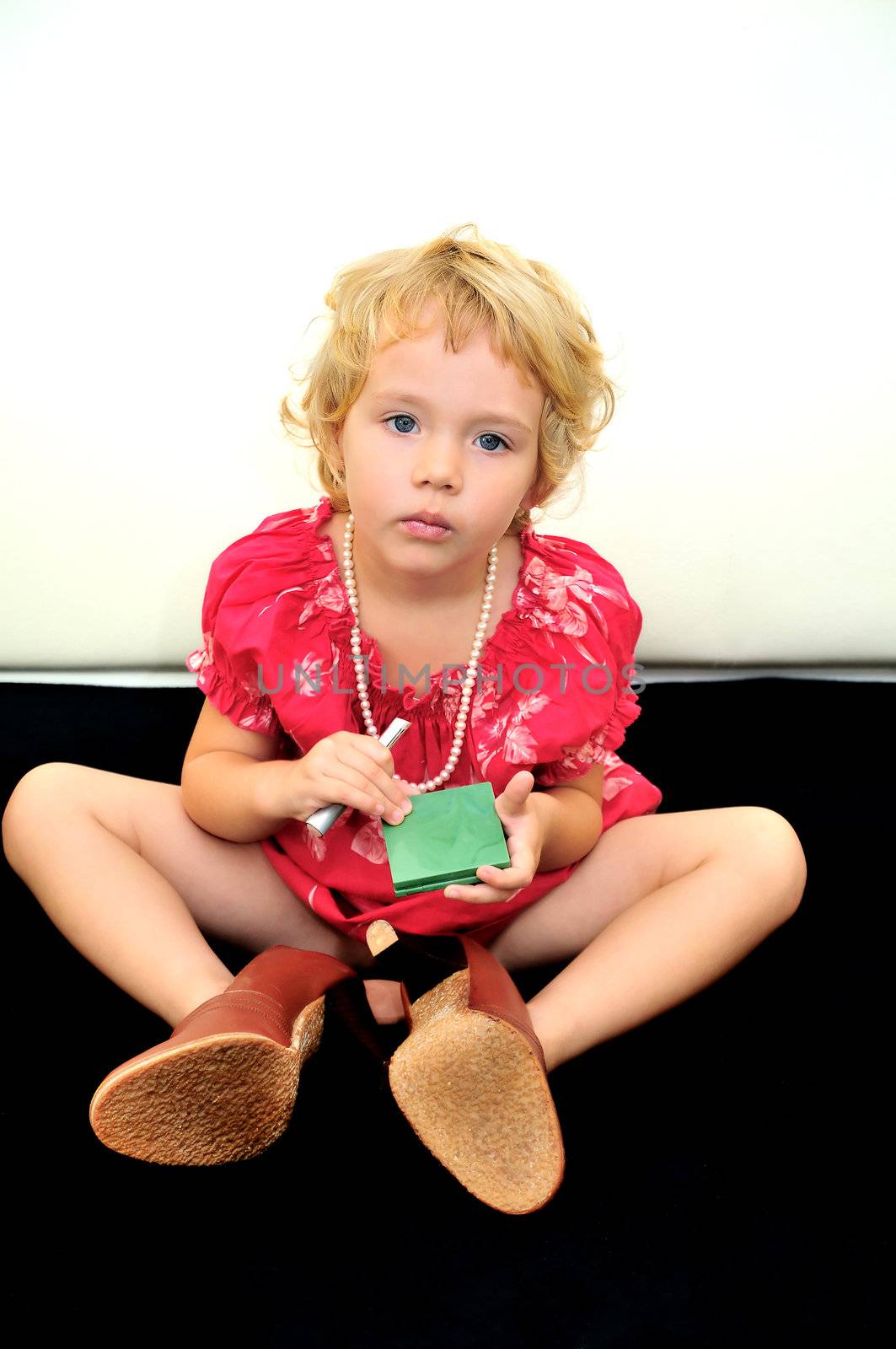 little girl using lipstick and powder, she is wearing necklace and high-heels mother's  shoes