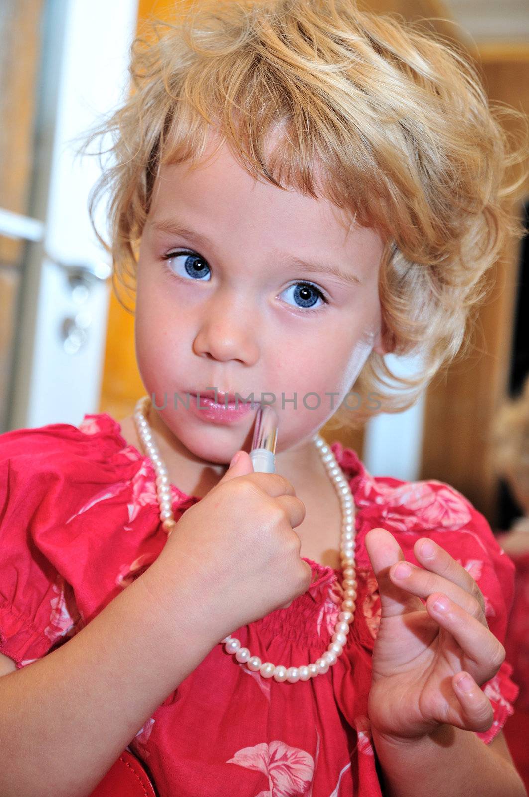 Little girl using lipstick, she is wearing necklace