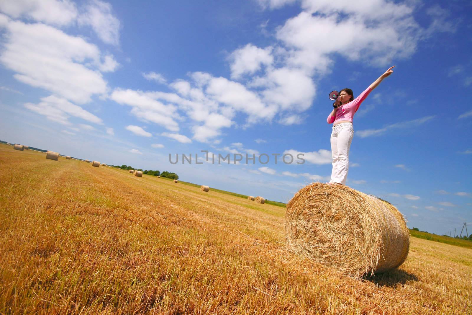 girl speaking through megaphone and pointing in field of hay bales 