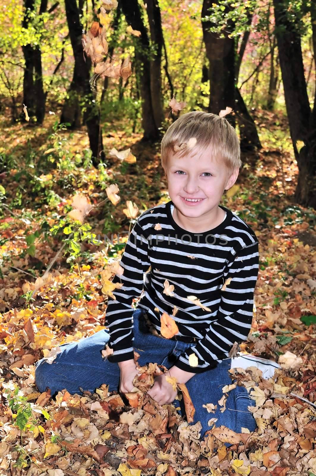 boy playing with yellow maple leaves in the forest.