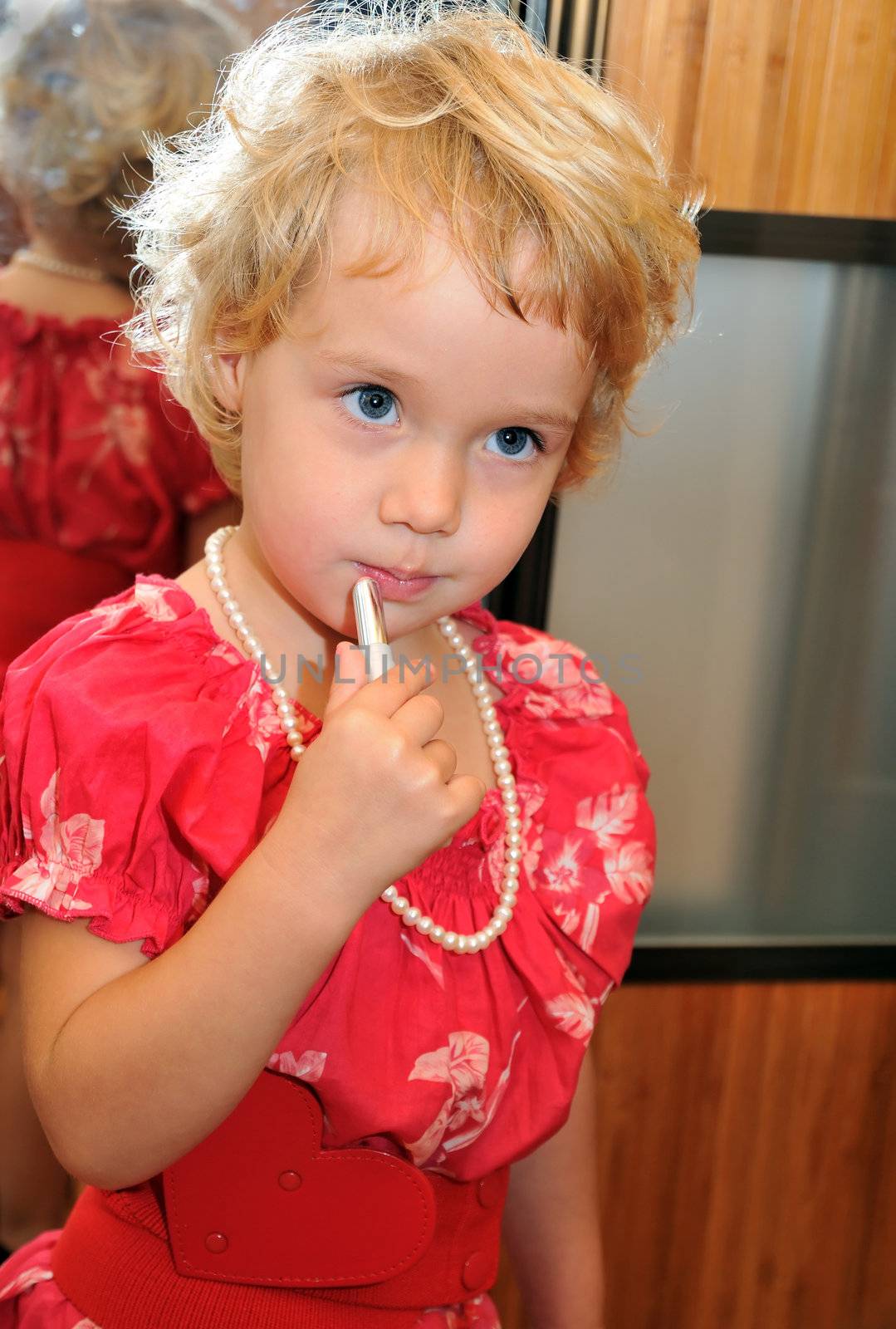 Little girl using lipstick, she is wearing necklace