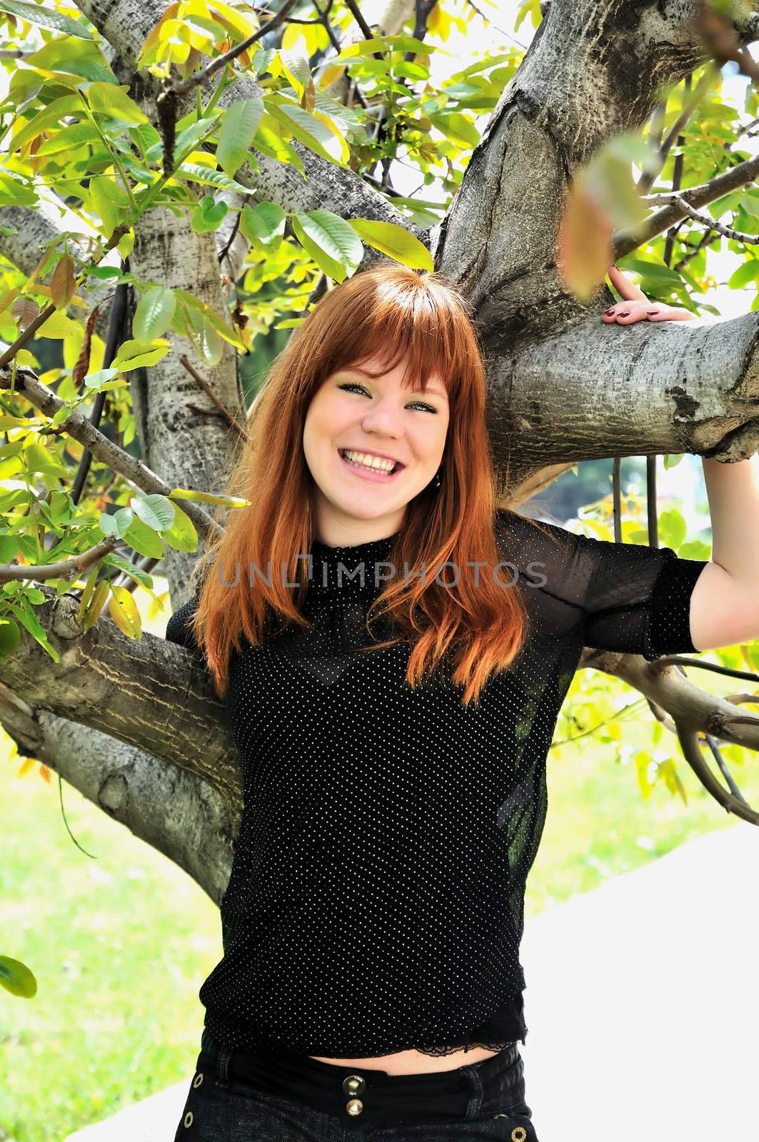 redhaired girl is standing under the tree and smiling