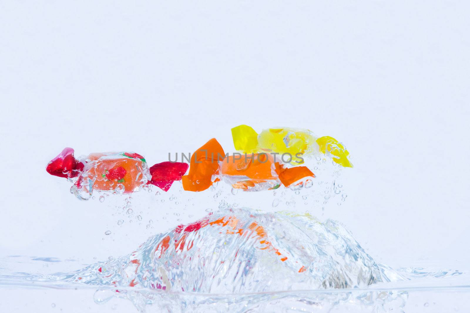 Splash of colorful fruit candies in the water with blue tint.