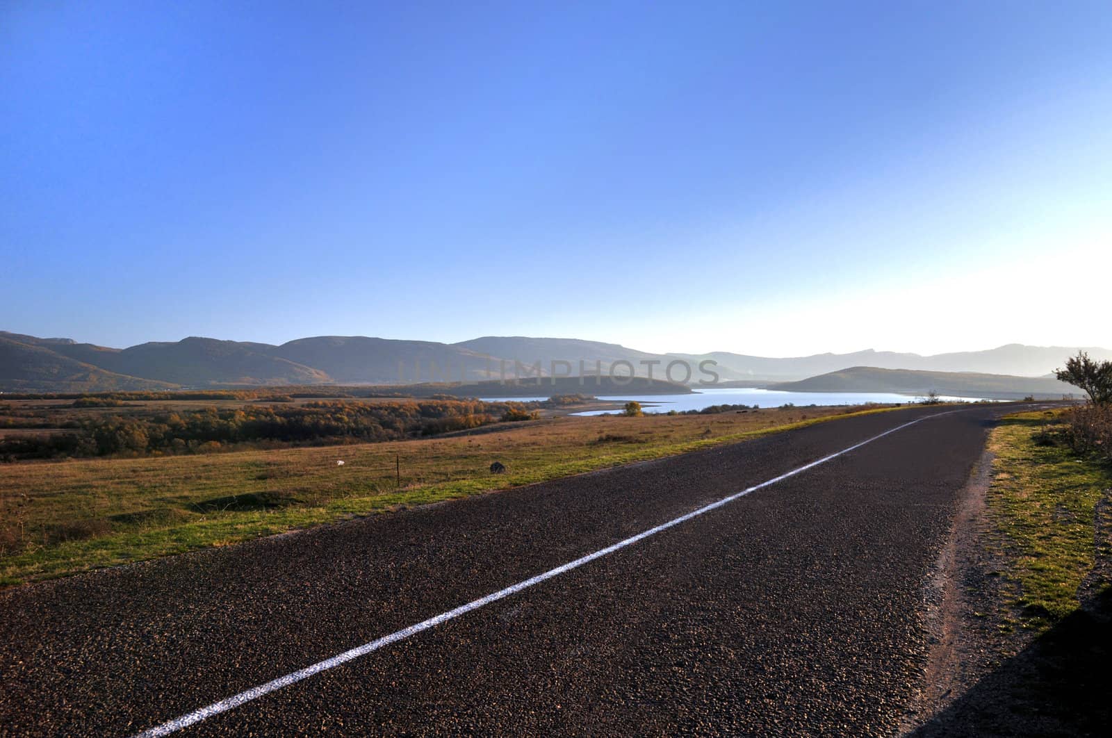 country road between lakes and autumn forest