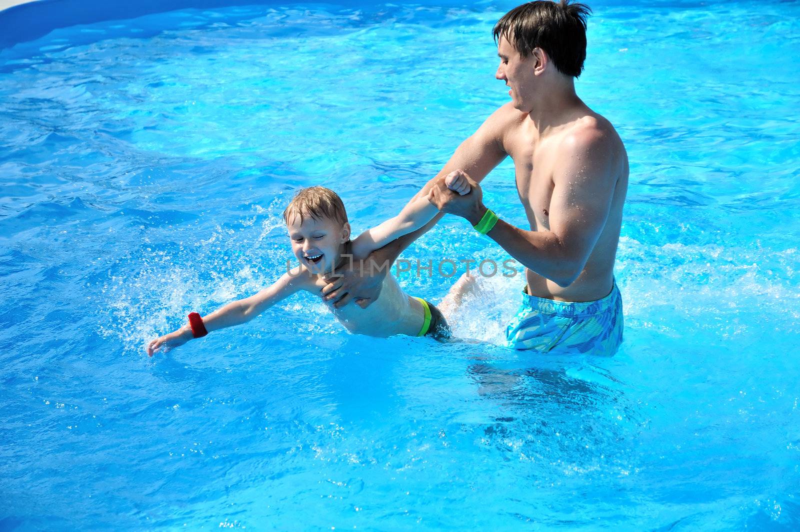  father teaching little boy to swim in the water pool
