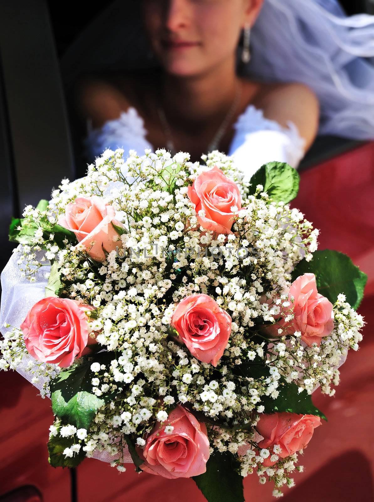 bride is sitting in the car and holding wedding pink flowers