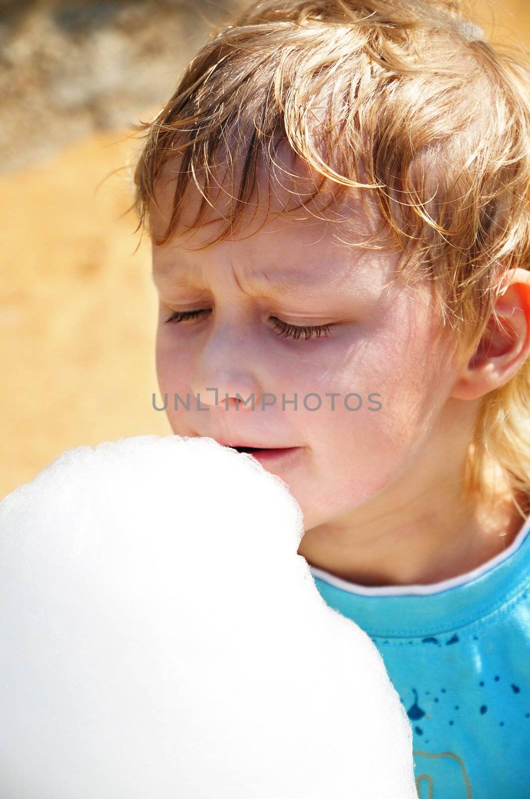  little boy is enjoying cotton candy in hot summer day

