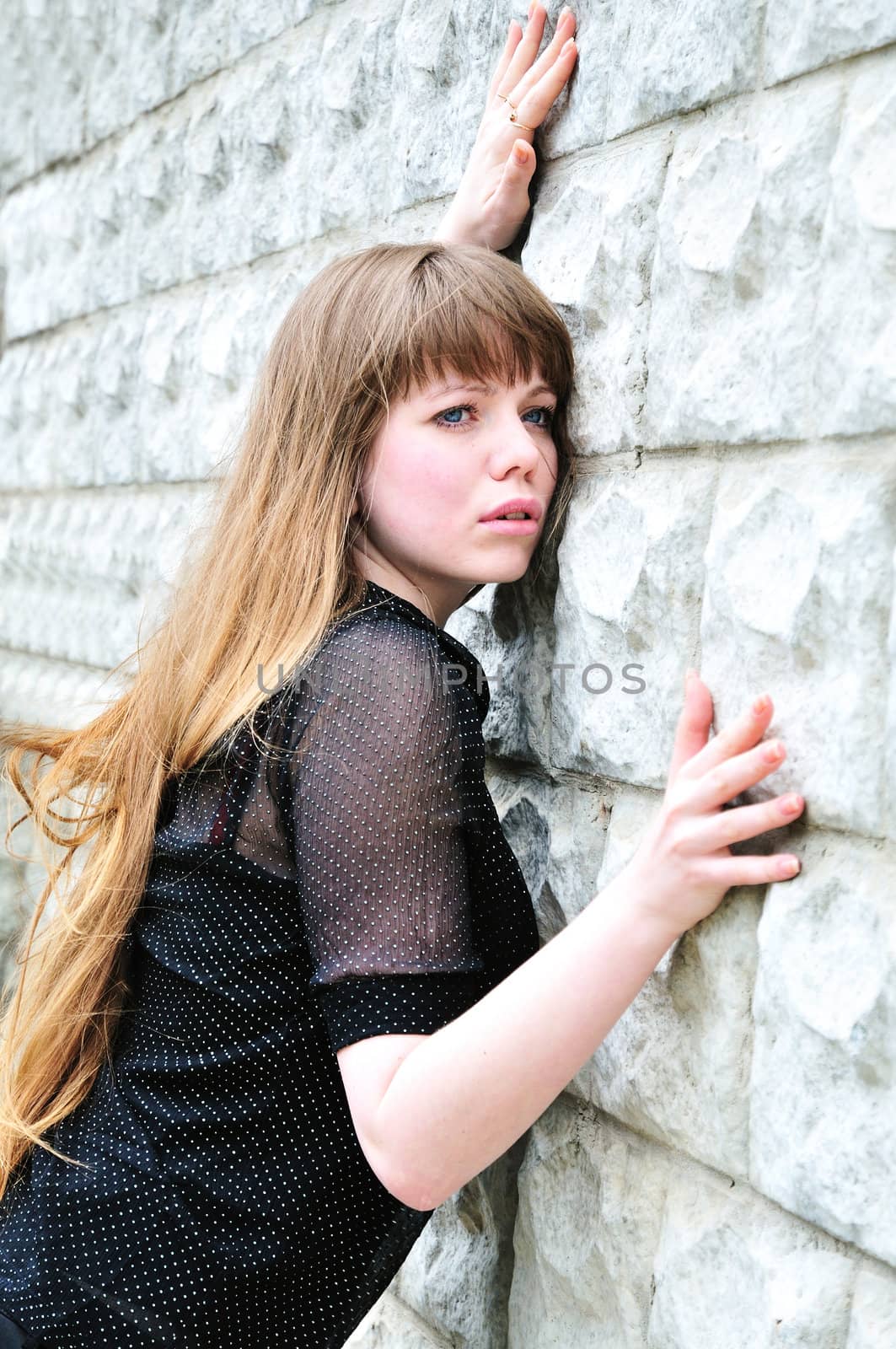 Blue-eyed long-haired girl leans on elbow wall 