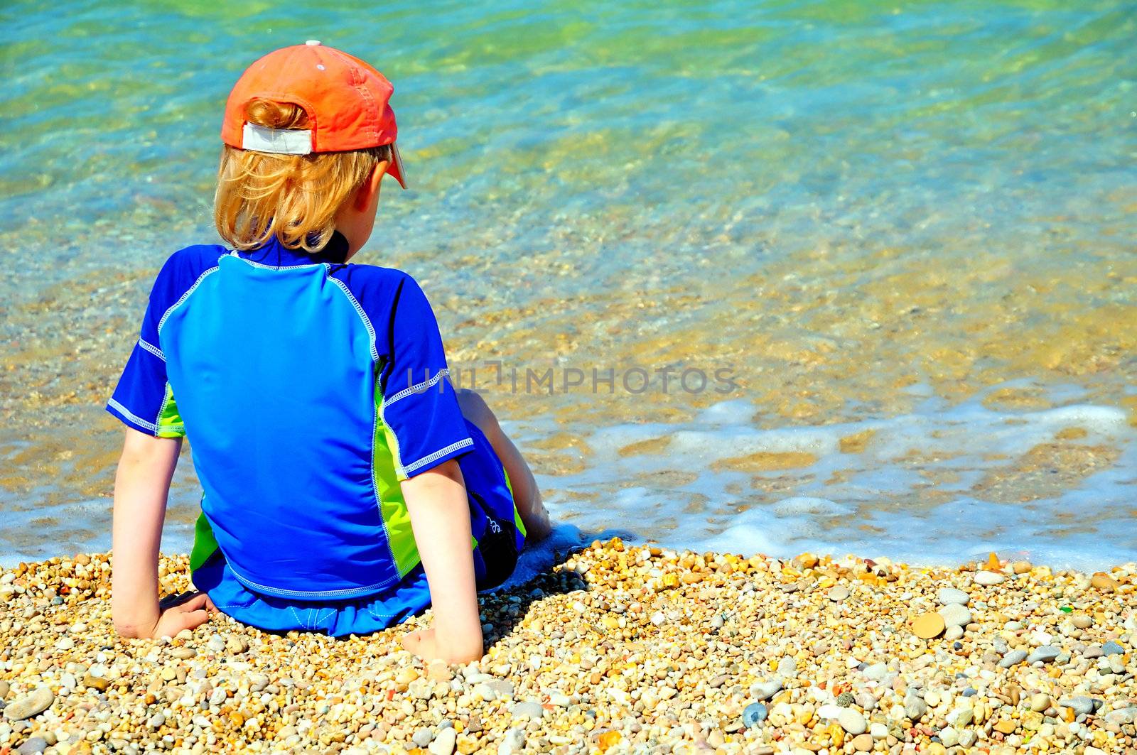 Boy looking at the sea and wetting legs water is still cold but he wants to swim