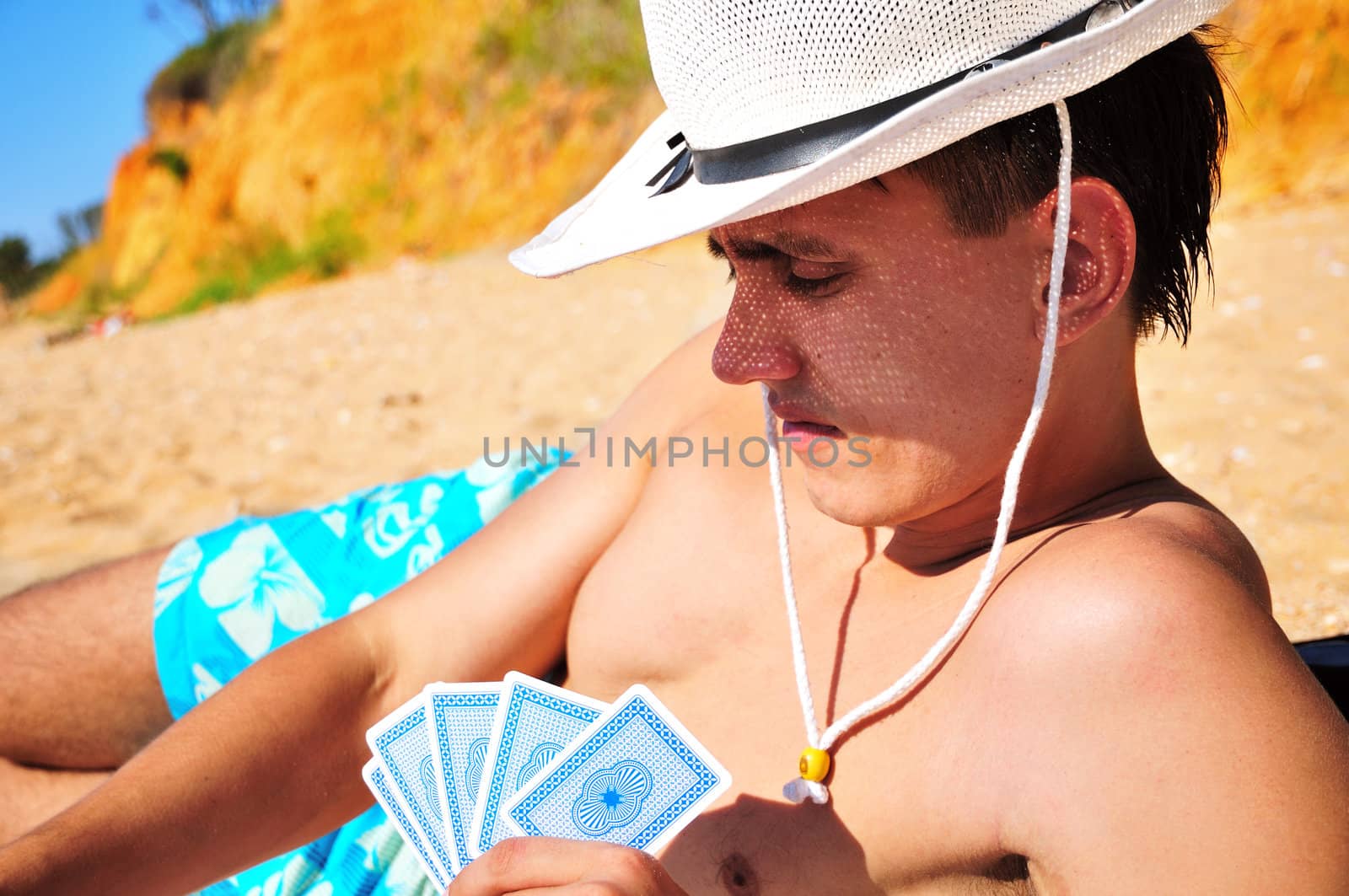 man wearing hat plying cards on the beach