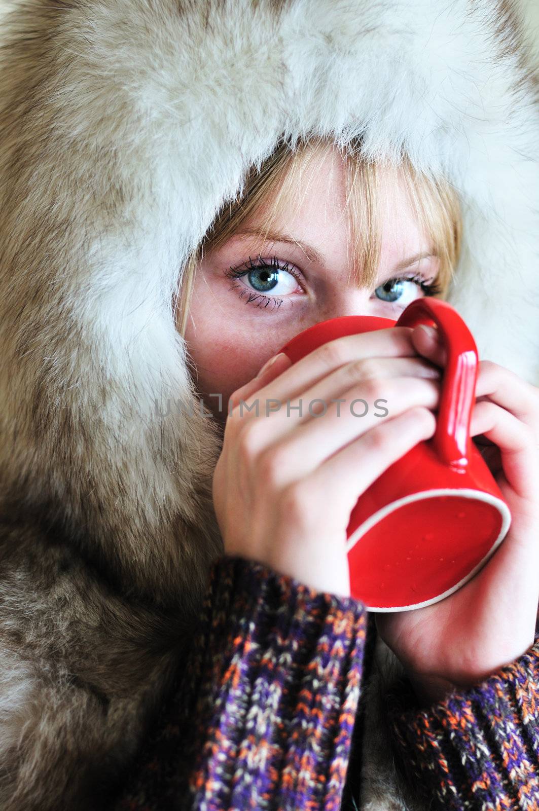 Girl in fur cap drinking tea from red cup
