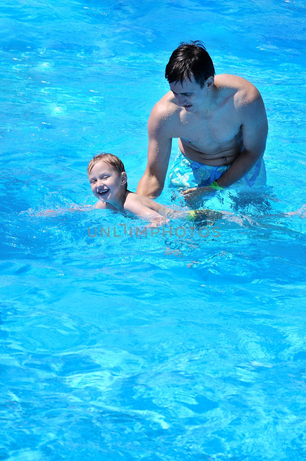 futher and son having fun in swimming pool, son is trying to swim