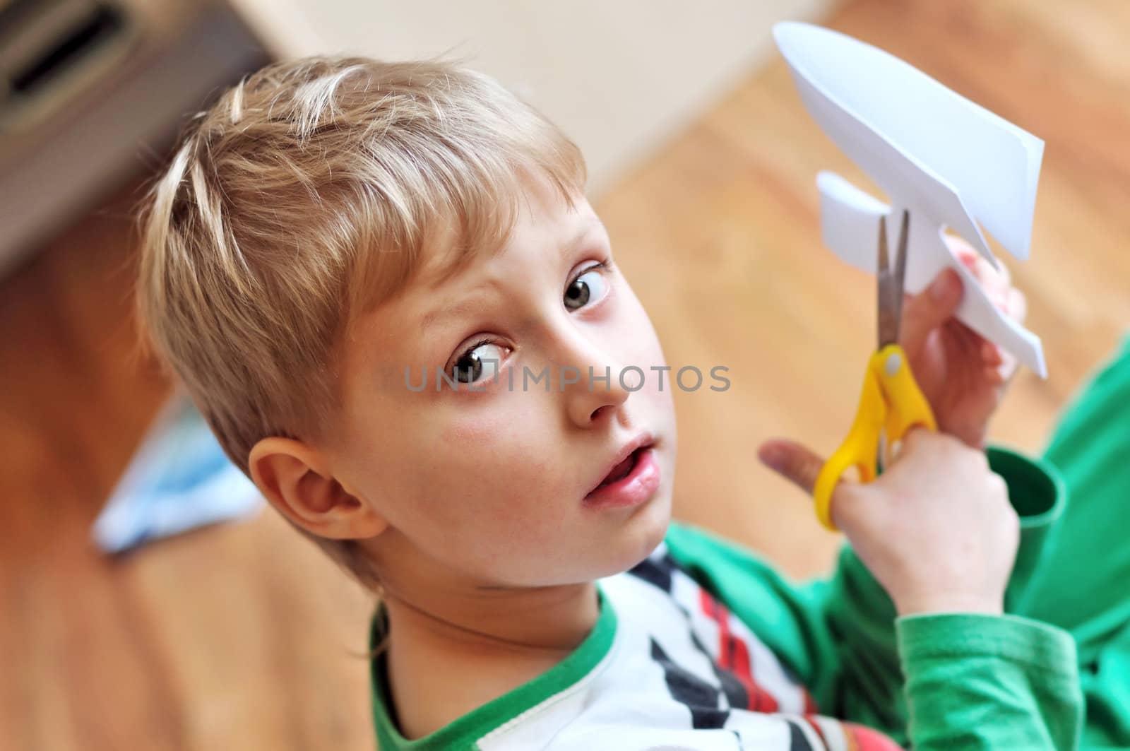little blond boy scissoring paper and looking at the camera