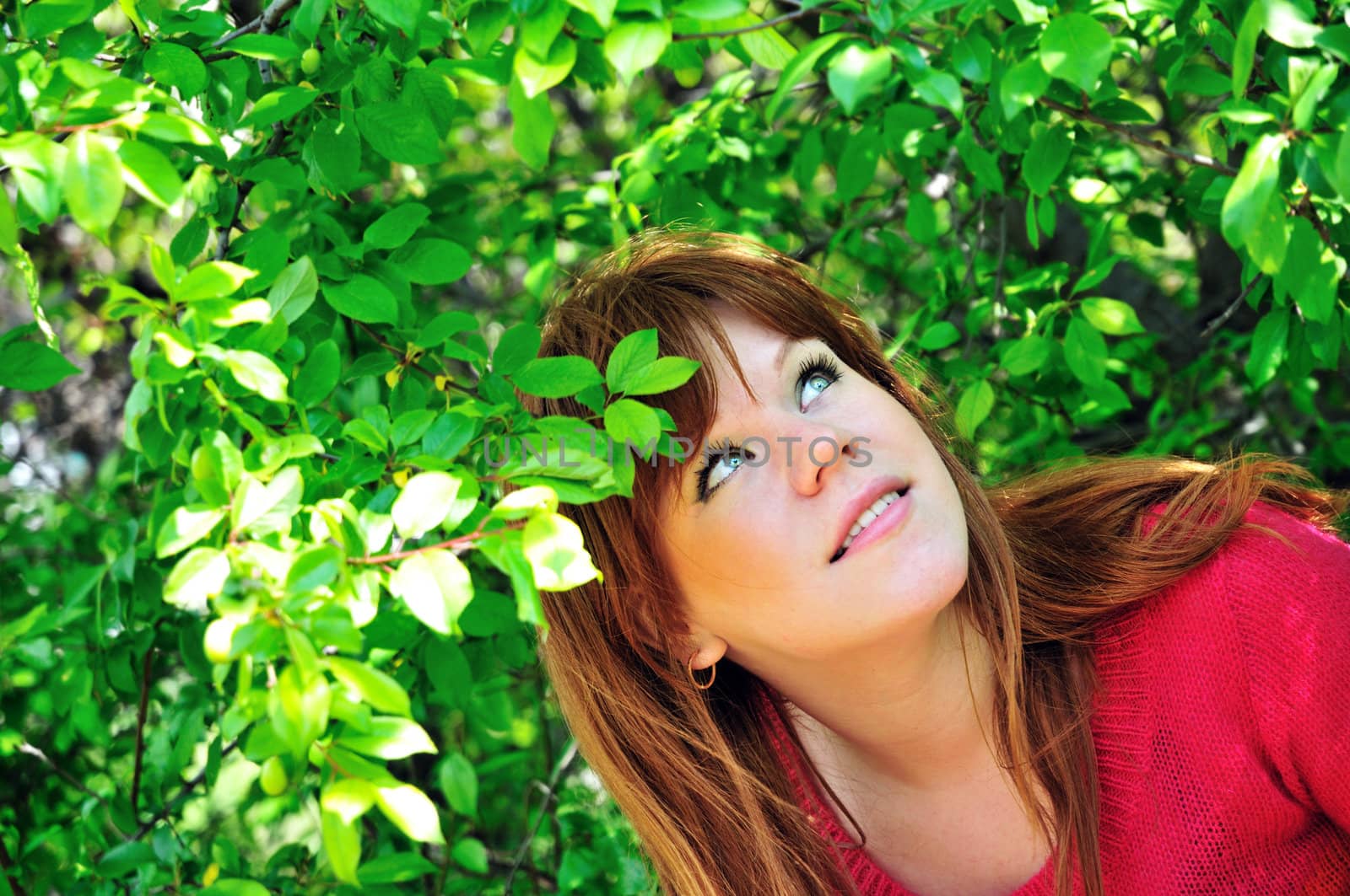 redheaded girl through green leaves in spring time