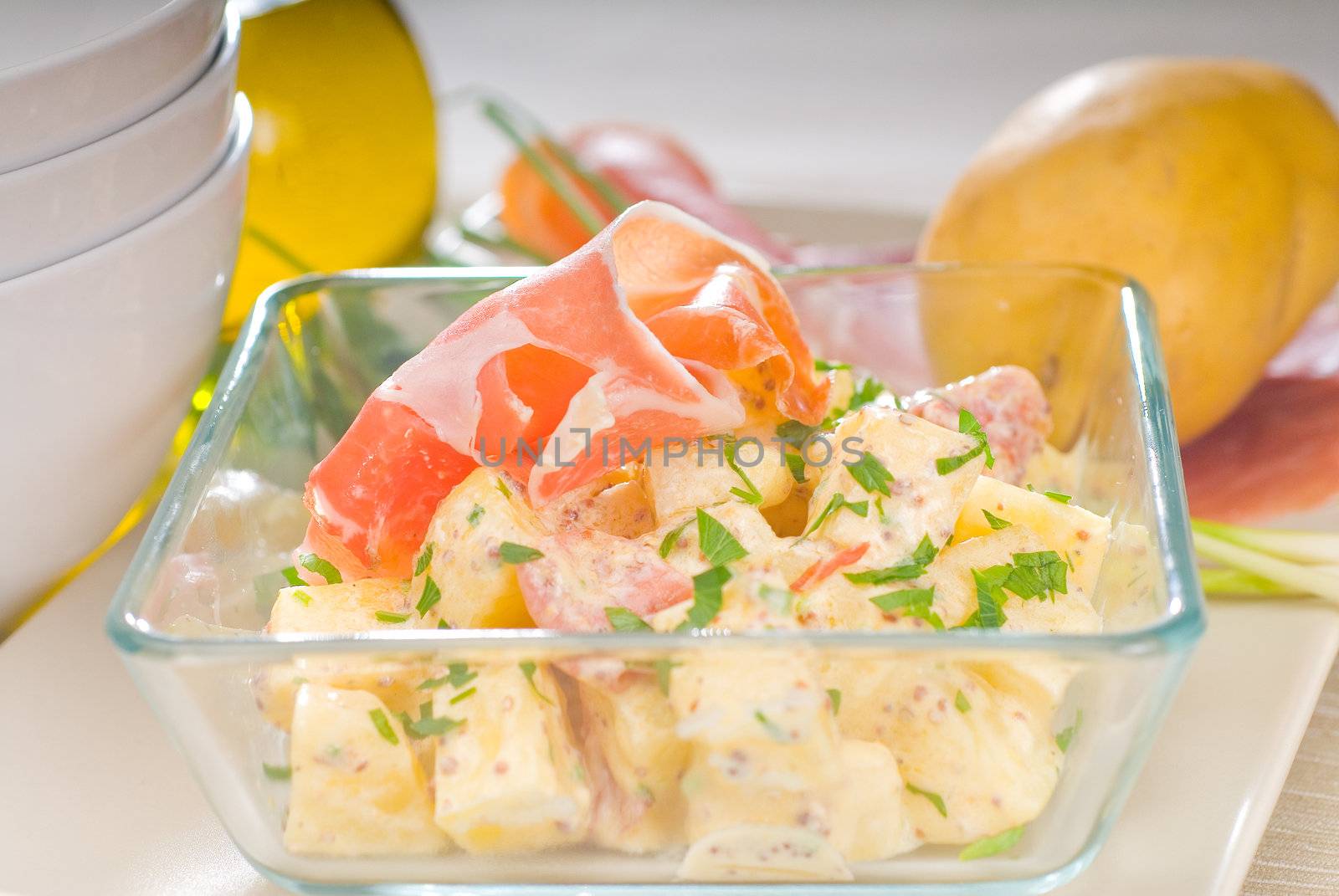 fresh home made parma ham and potato salad,with raw ingredients around with bowls and dishware on a table