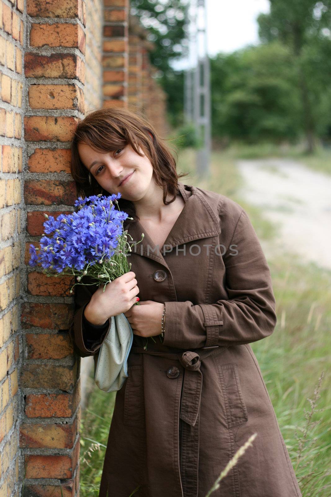 Young woman with flowers, near the wall
