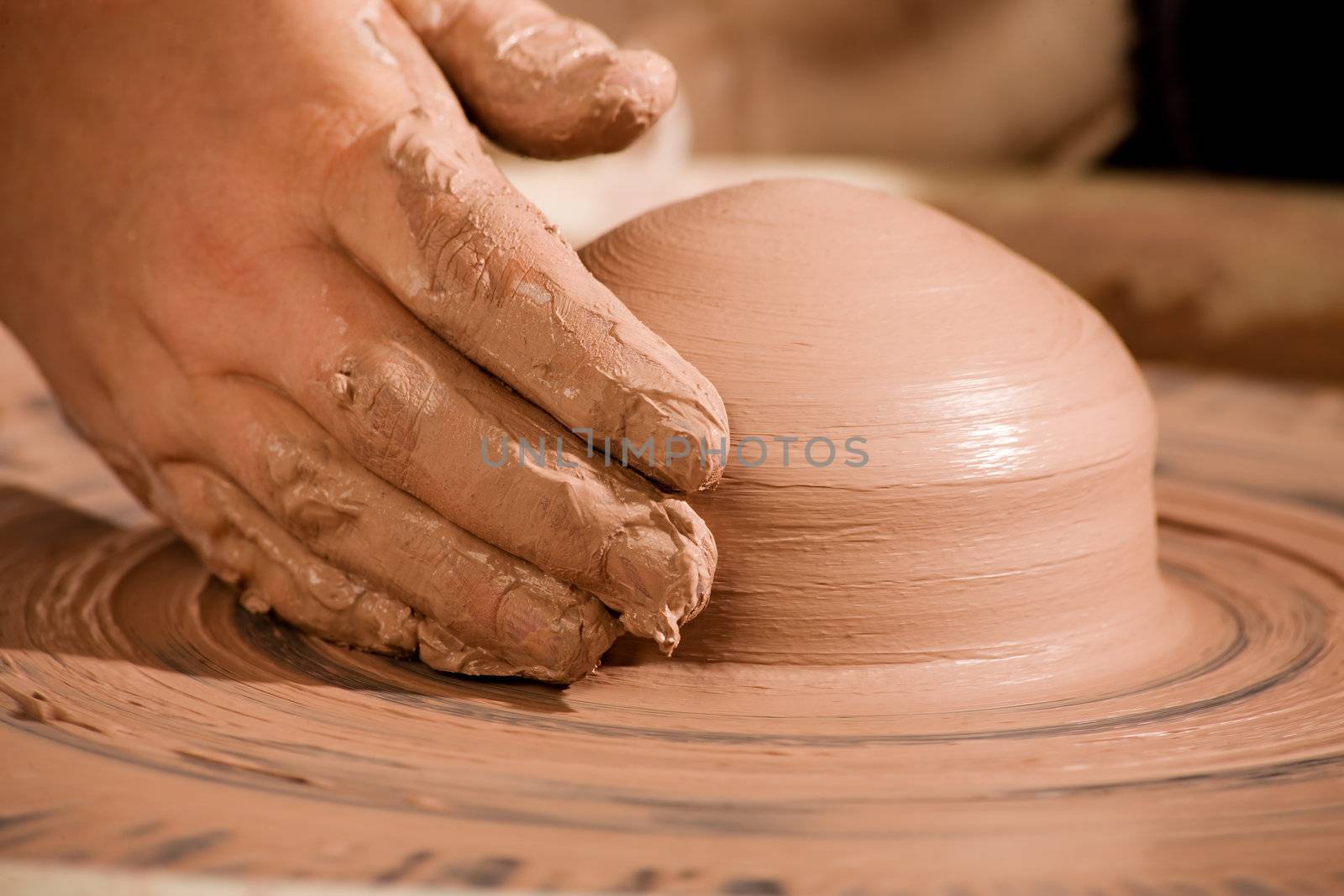 Hand shaping wedge of clay on spinning potters wheel