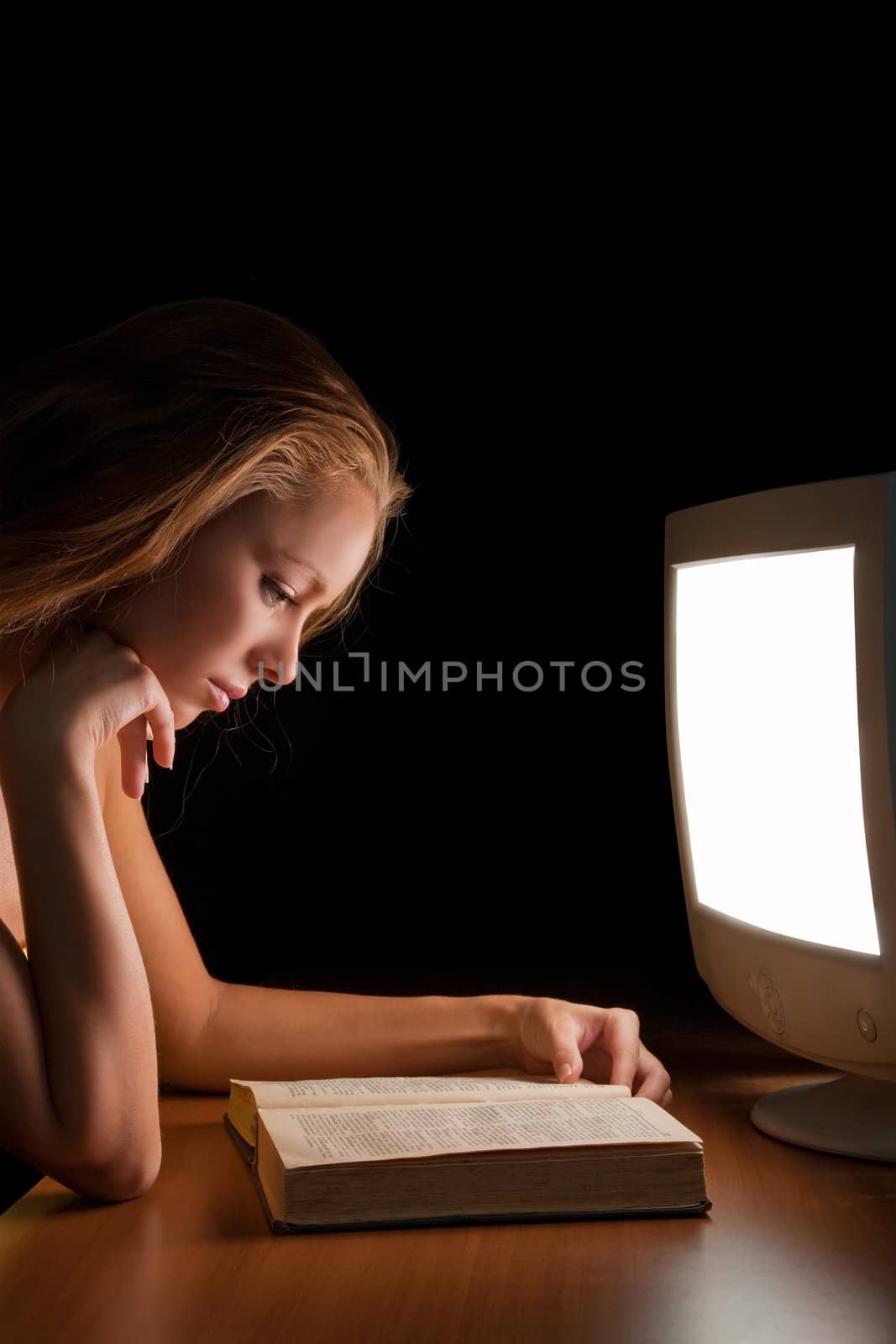 girl reading a book (textbook) in the light of a working computer