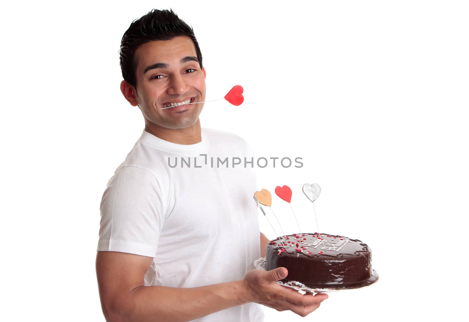 A man holds a chocolate mud cake decorated with love hearts.   He has a red love heart clenched between his teeth.  Suitable for birthday or special occasion.
